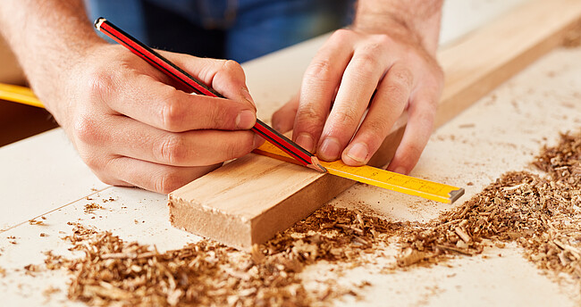 Arbeiten und Bauen mit Holz Ein Zollstock und ein Stück Holz, jemand zeichnet etwas ein