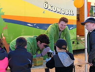 FÖJler bei der Arbeit Zwei FÖJler gucken durch Mikroskope, daneben stehen interessierte Kinder